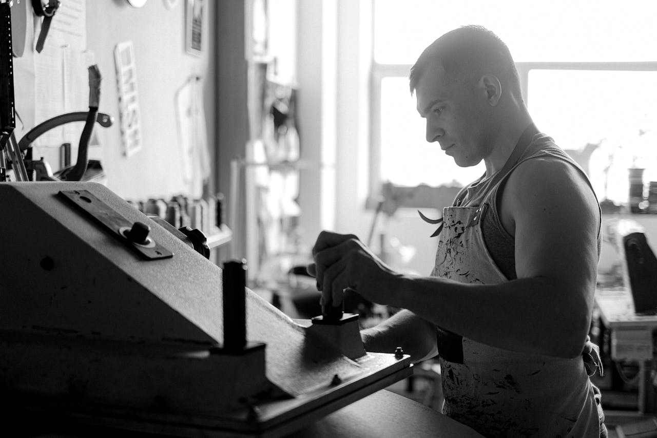 Offerings Black and white photo of a leather artisan working indoors with machinery.